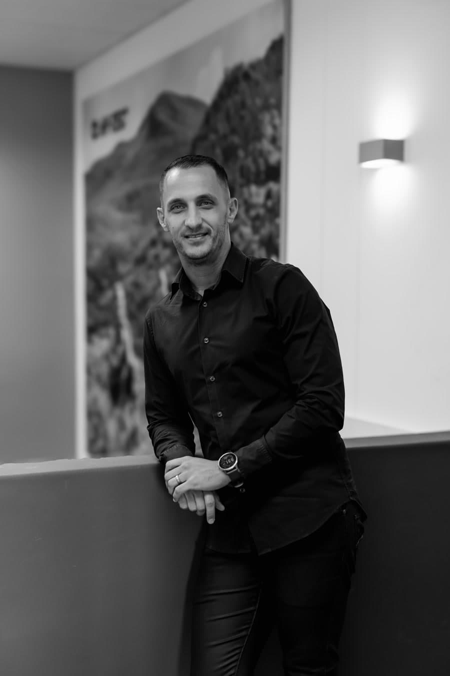Edson Cloete, founder of ASPIYRE, in a black shirt, leaning on a ledge in an office.
